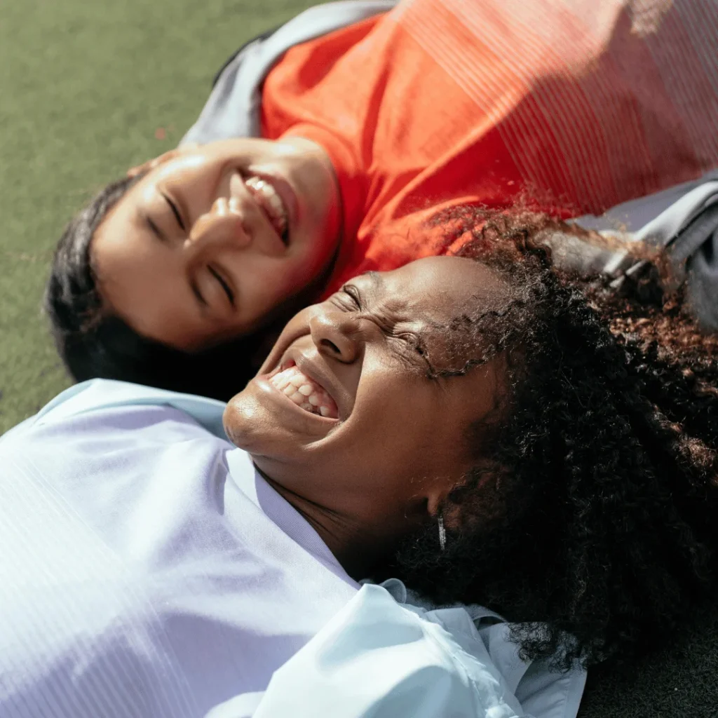 two young girls smiling whilst lying down on grass